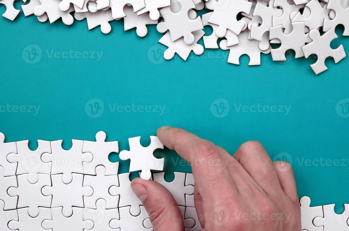 The hand folds a white jigsaw puzzle and a pile of uncombed puzzle pieces lies against the background of the blue surface. Texture photo with space for text