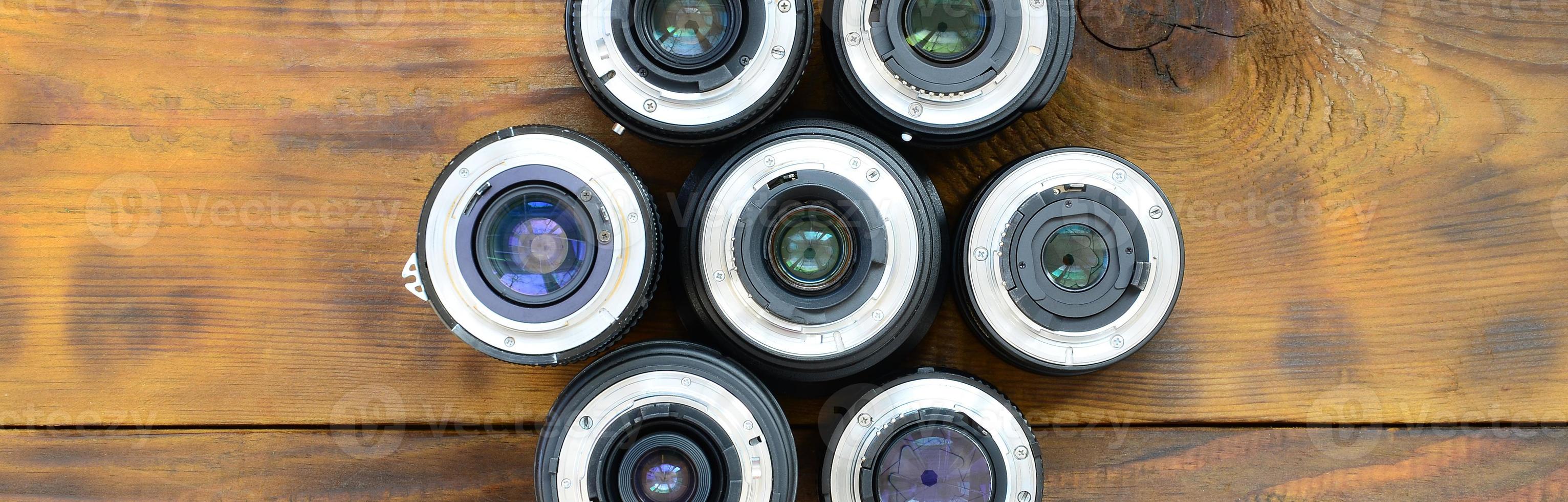 Several photographic lenses lie on a brown wooden background. Space for text photo