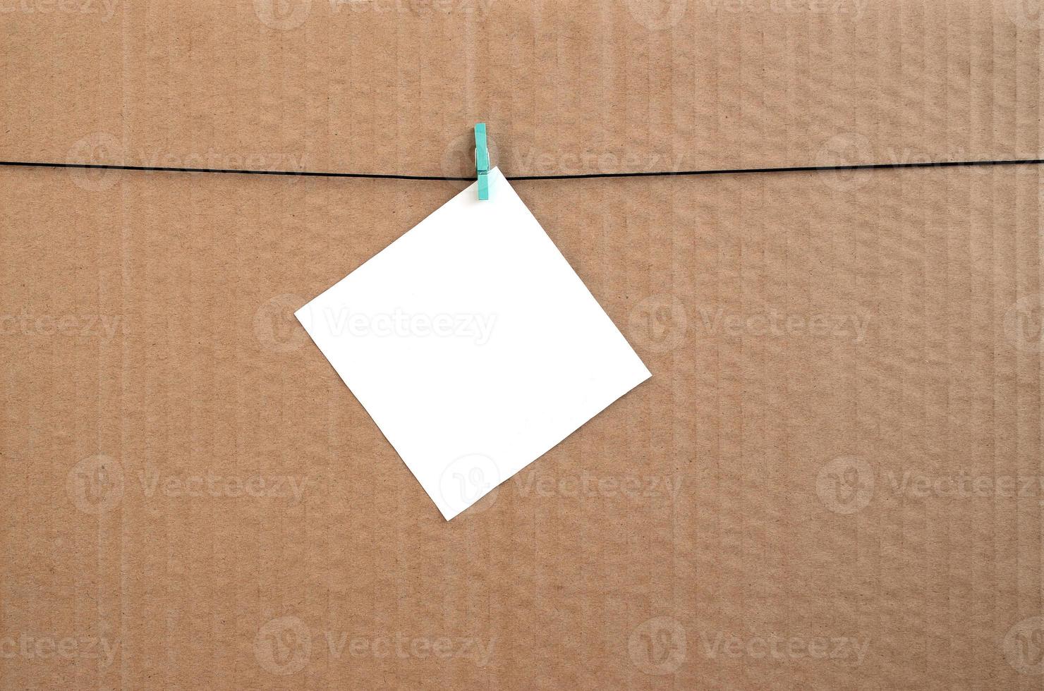 White blank card on rope on a brown cardboard background. Creative reminder, small sheet of paper on wooden clothespin, memo backdrop photo