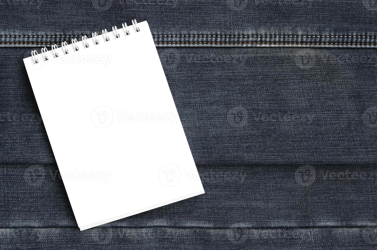 White notebook with clean pages lying on dark blue jeans background. Image with copy space photo