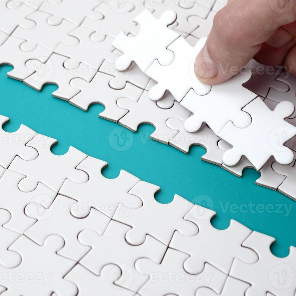The human hand paves the way to the surface of the jigsaw puzzle, forming a blue space. The concept of overcoming the difficulties on the way to success photo