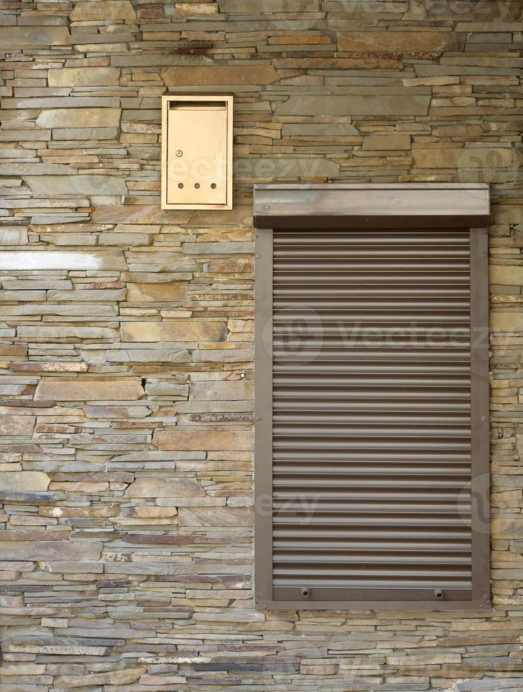 A window with brown metal rolling shutters and wall decoration with artificial stone photo