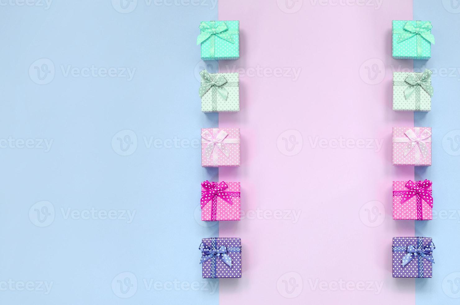 Small gift boxes of different colors with ribbons lies on a violet and pink background photo