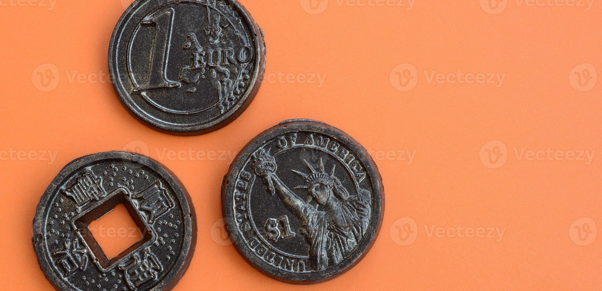 Three chocolate products in the form of Euro, USA and Japan coins lie on an orange plastic background. A model of cash coins in an edible form photo