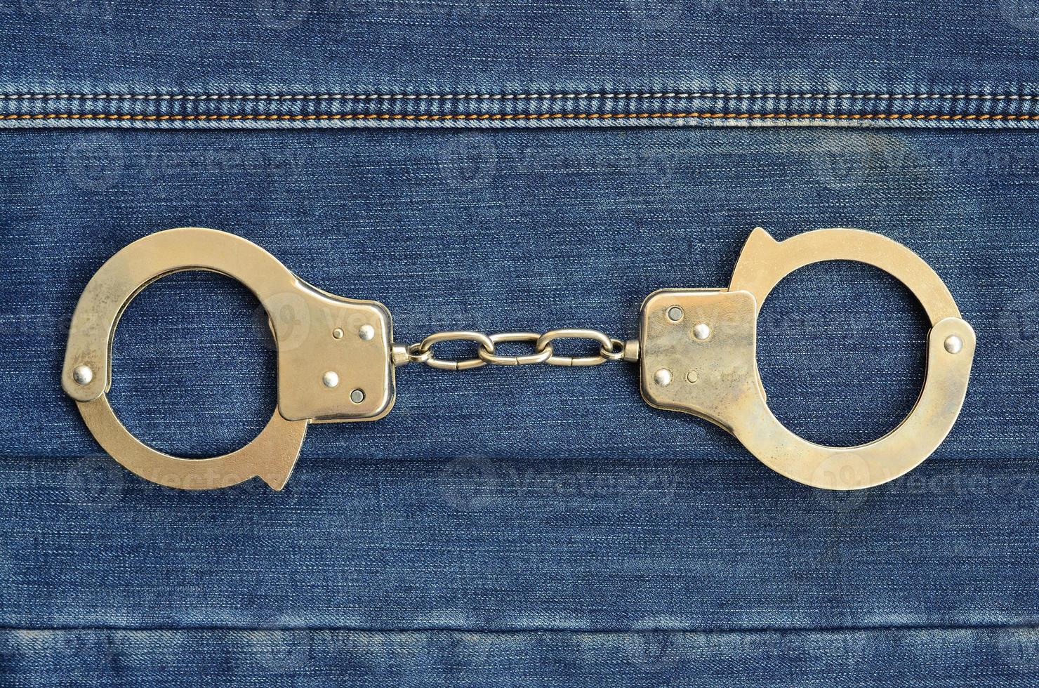 Police steel handcuffs lying on dark blue jeans background photo