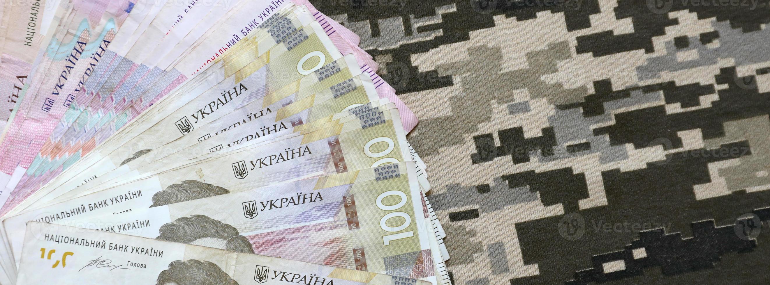 Ukrainian hryvnya bills on fabric with texture of Ukrainian military pixeled camouflage. Cloth with camo pattern in grey, brown and green pixel shapes photo