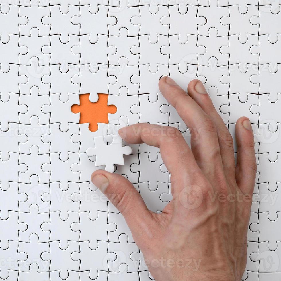 The texture of a white jigsaw puzzle in the assembled state with one missing element that the male hand puts in photo