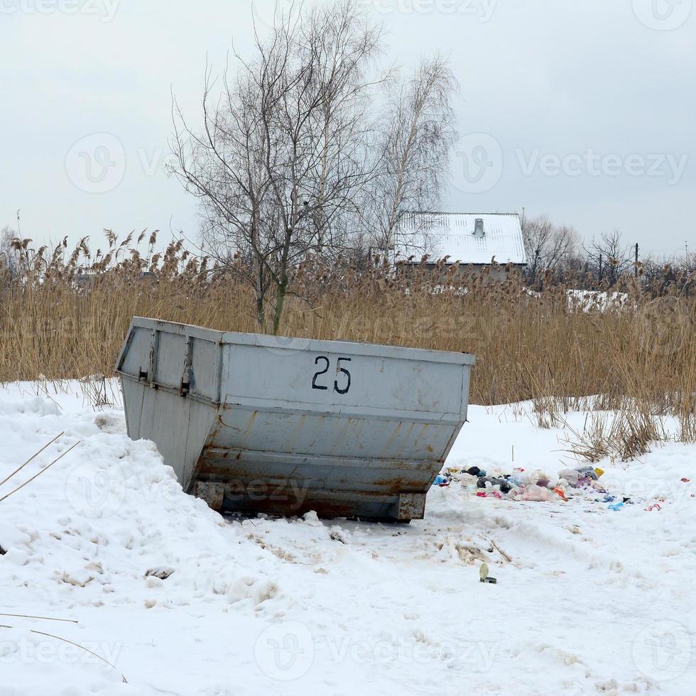 Trash bin at the side of street in winter with lip garbage container winter snow. Metal container for household waste photo