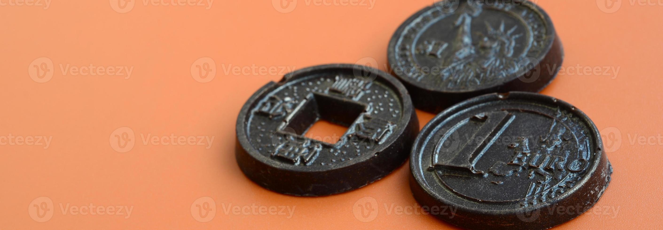 Three chocolate products in the form of Euro, USA and Japan coins lie on an orange plastic background. A model of cash coins in an edible form photo