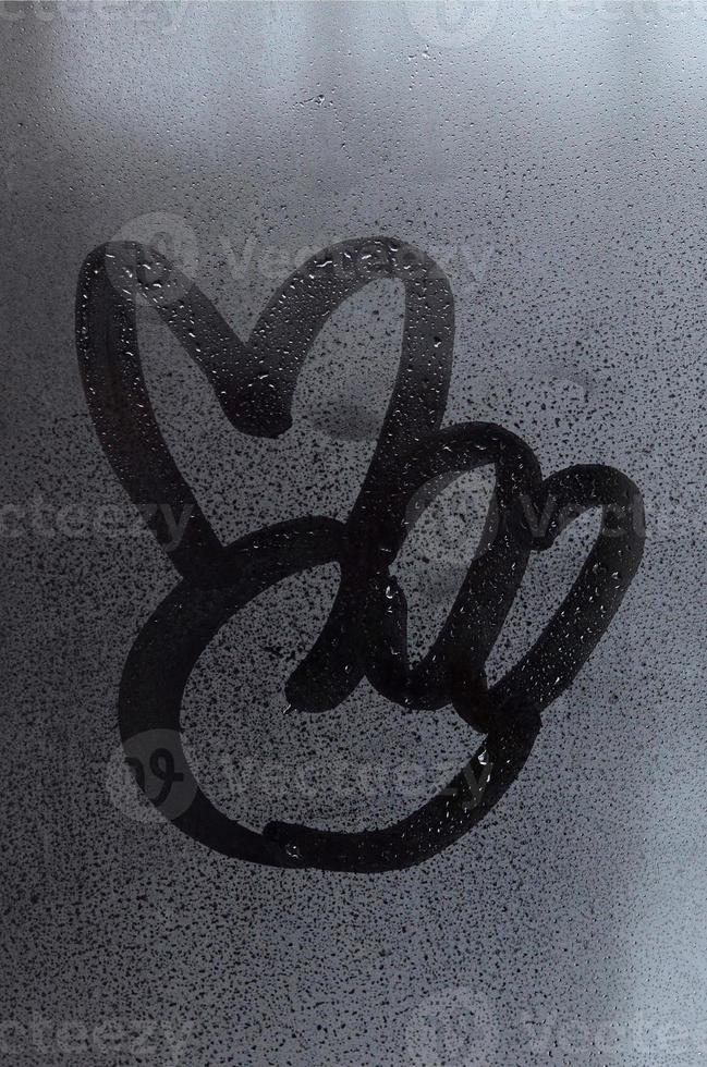 The image of the peace symbol is drawn with a finger on the surface of a misted glass window. Combination of two fingers photo