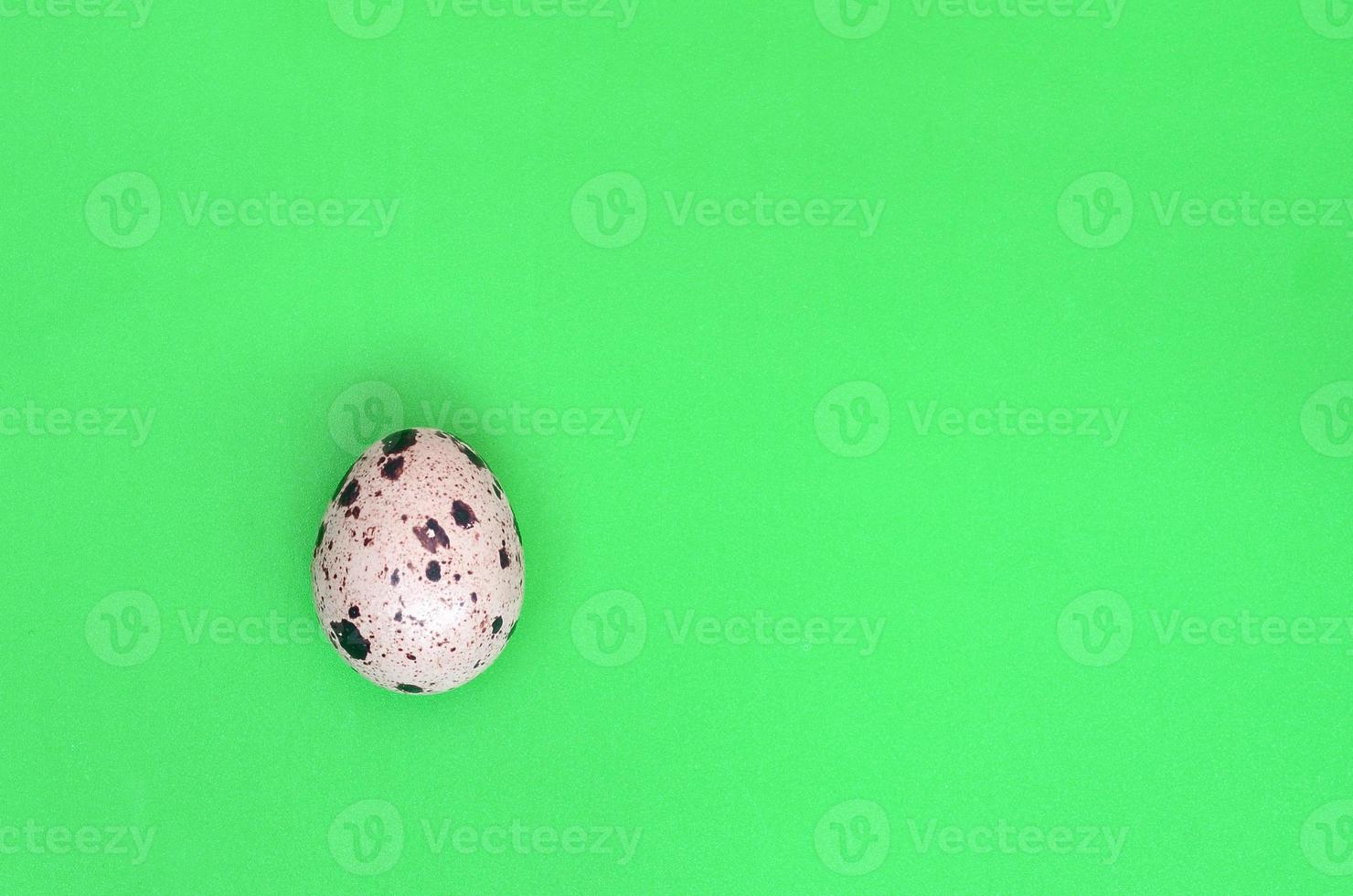 One quail egg on a light green surface, top view, empty place fo photo