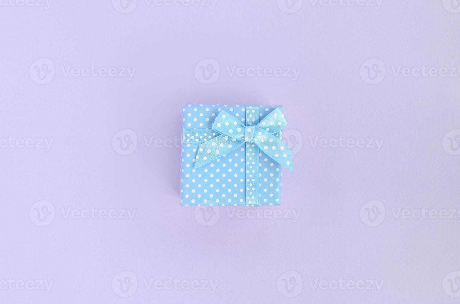 Small blue gift box with ribbon lies on a violet background. Minimalism flat lay top view photo