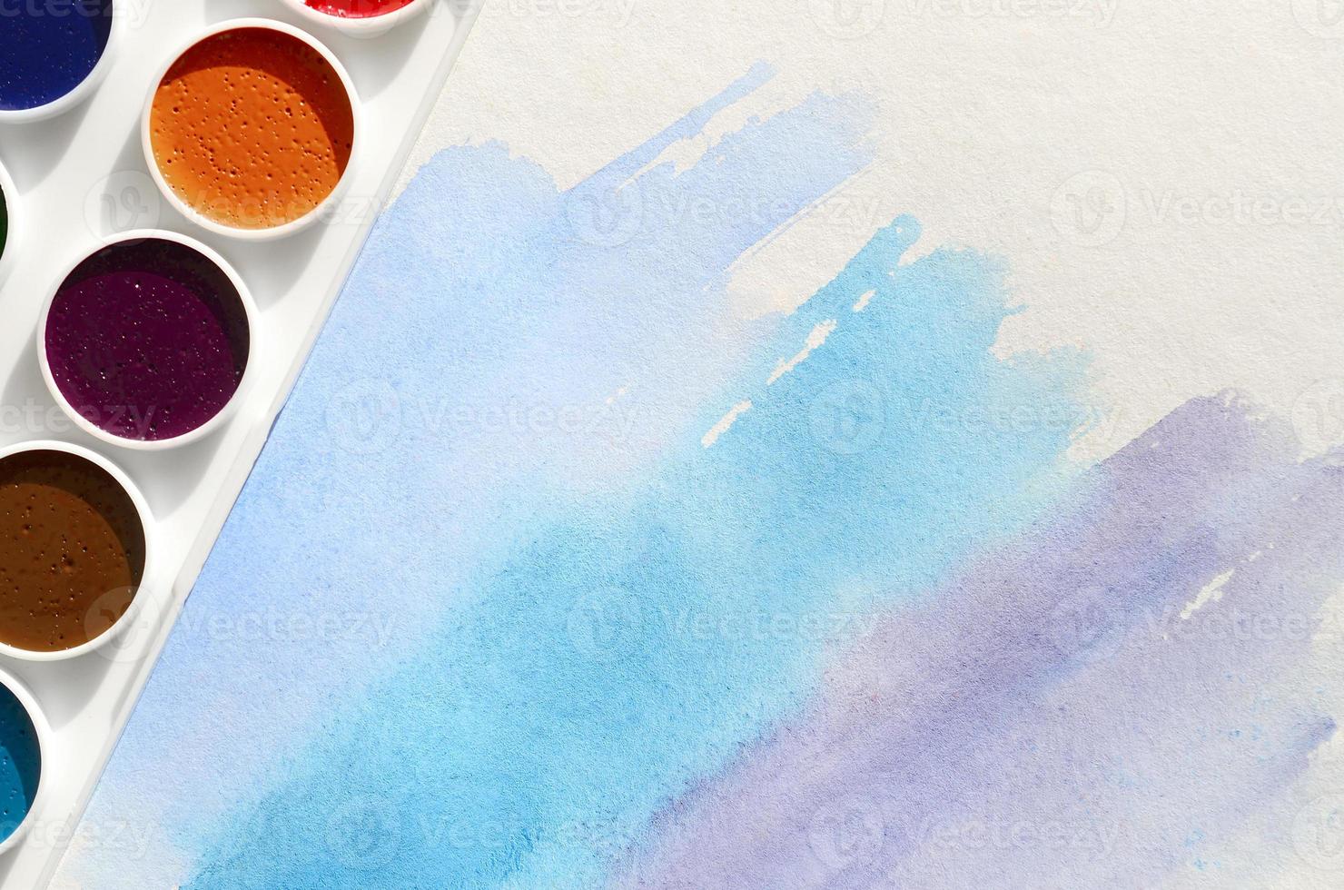 A new set of watercolors lies on a sheet of paper, which shows an abstract watercolor drawing in the form of blue strokes. The concept of amateur painting among teenagers photo