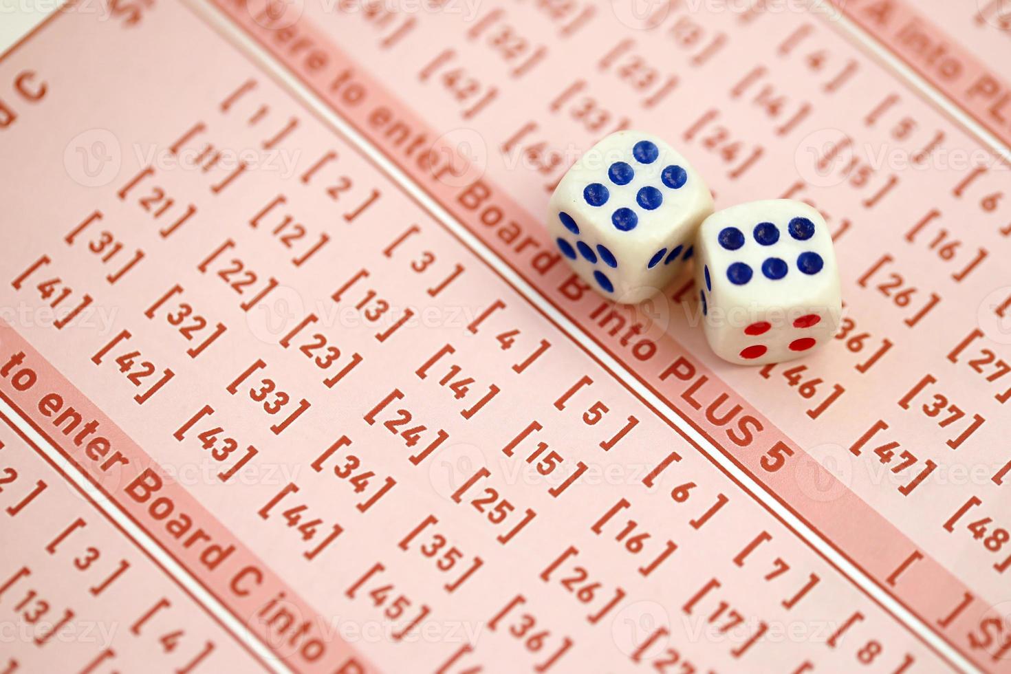Dice cubes lies on pink gambling sheets with numbers for marking to play lottery. Lottery playing concept or gambling addiction. Close up photo