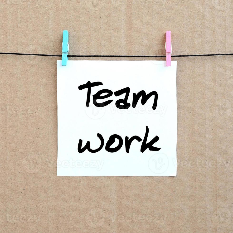 Team work. Note is written on a white sticker that hangs with a clothespin on a rope on a background of brown cardboard photo