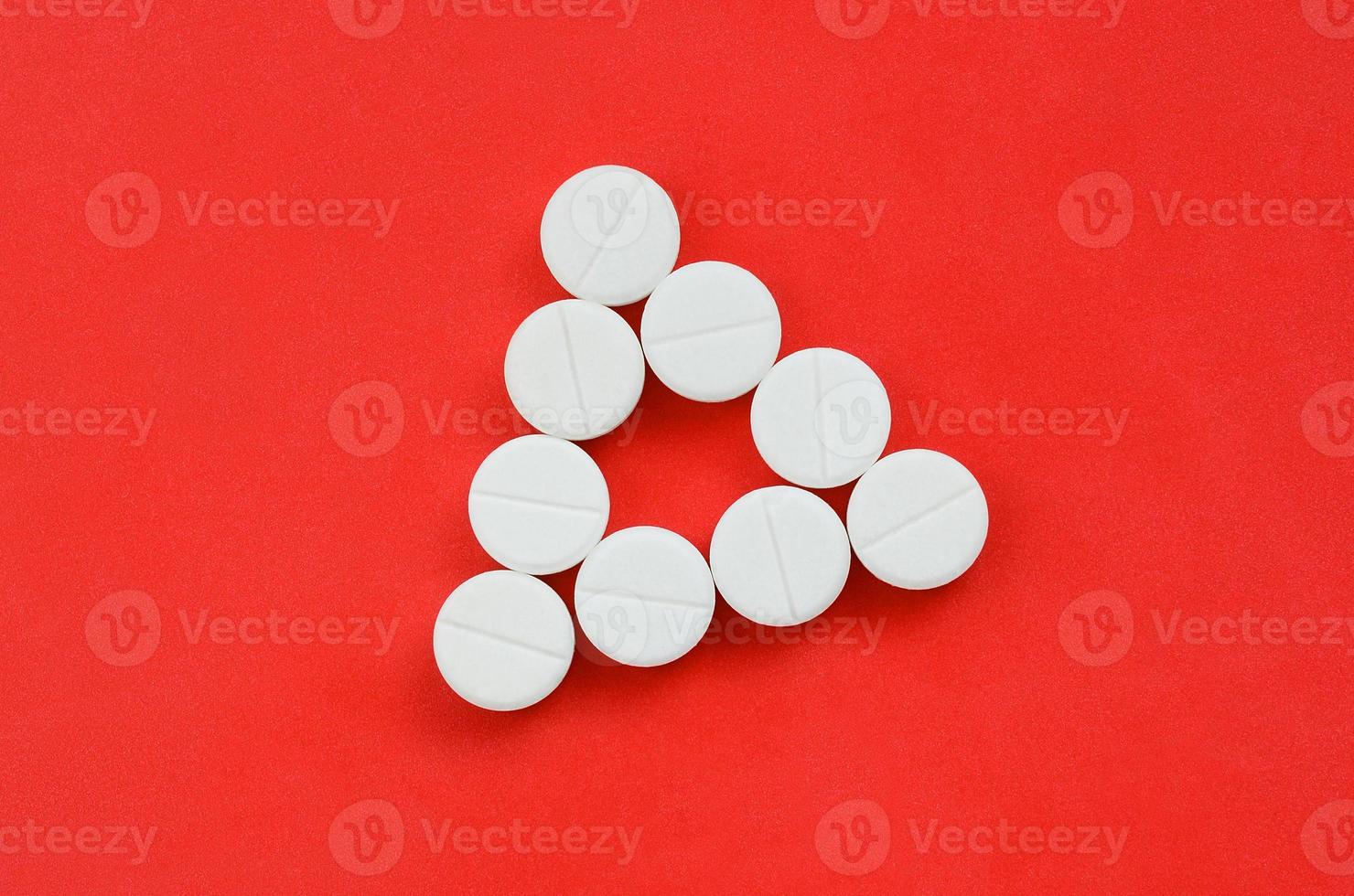 Several white tablets lie on a bright red background in the form of an even triangle. Background image on medicine and pharmaceutical topics photo