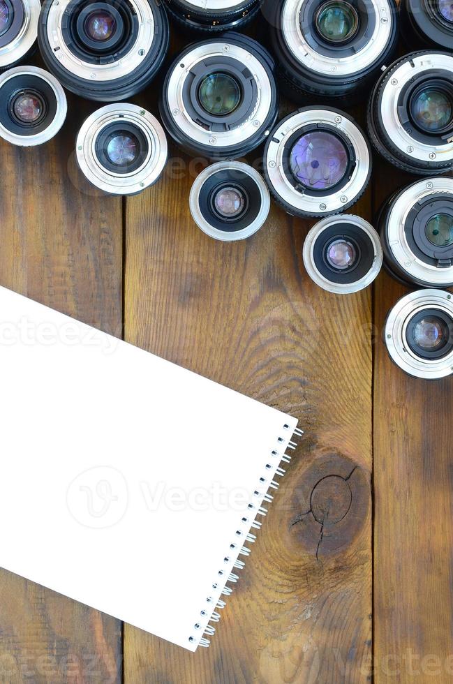 Several photographic lenses and white notebook lie on a brown wooden background. Space for text photo