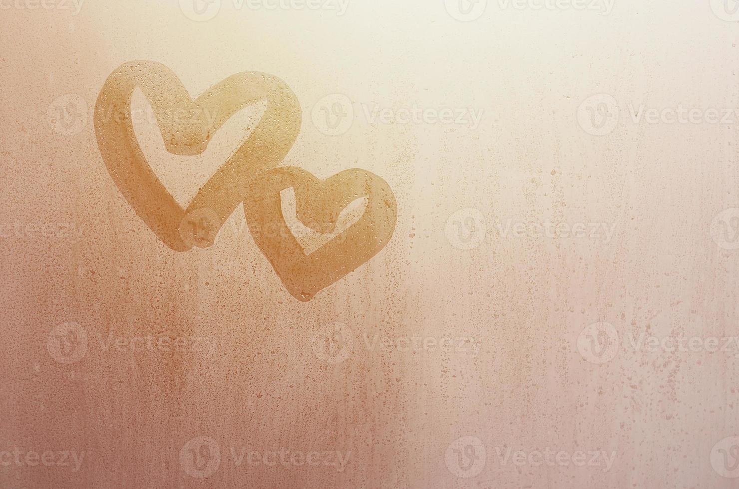 Couple of abstract blurred love heart symbol drawn by hand on the wet window glass with sunlight background. Template for Valentine Day postcards photo