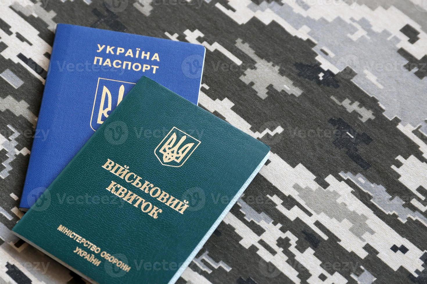 Ukrainian military ID and foreign passport on fabric with texture of pixeled camouflage. Cloth with camo pattern in grey, brown and green shapes with Ukrainian army personal token and passport. photo