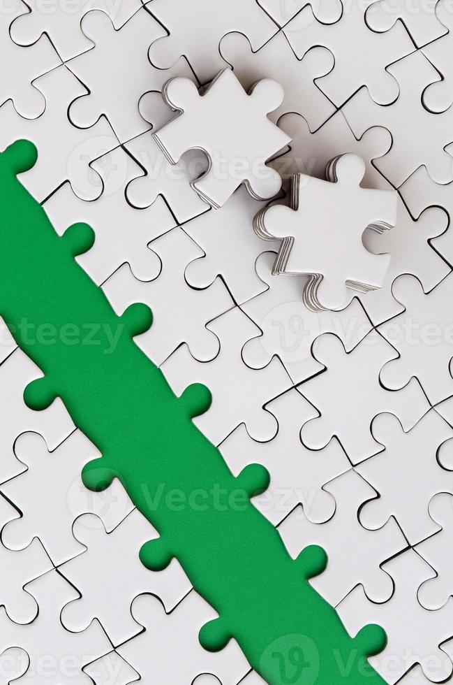 The green path is laid on the platform of a white folded jigsaw puzzle. The missing elements of the puzzle are stacked nearby. Texture image with space for text photo