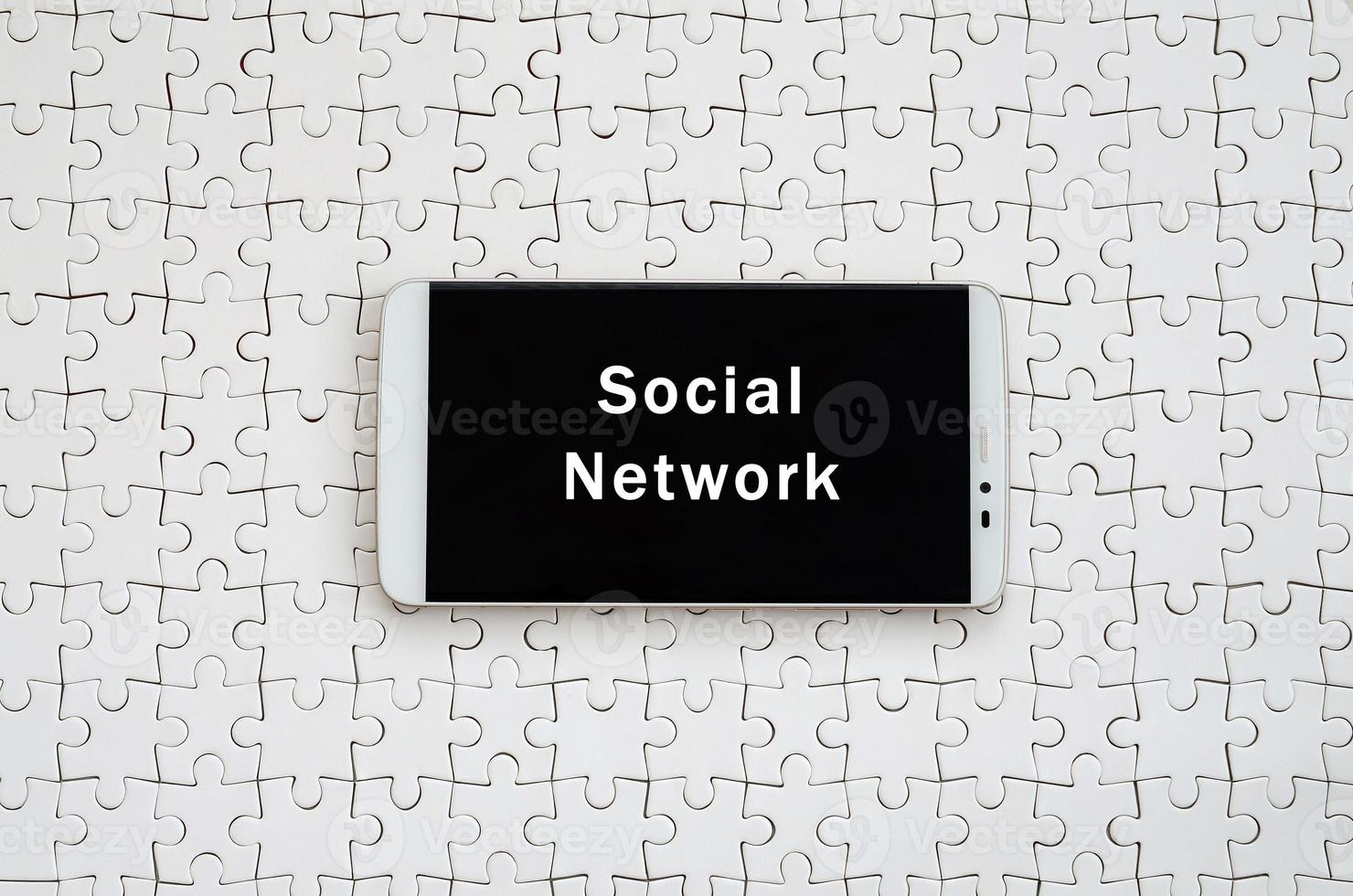 A modern big smartphone with a touch screen lies on a white jigsaw puzzle in an assembled state with inscription. Social network photo