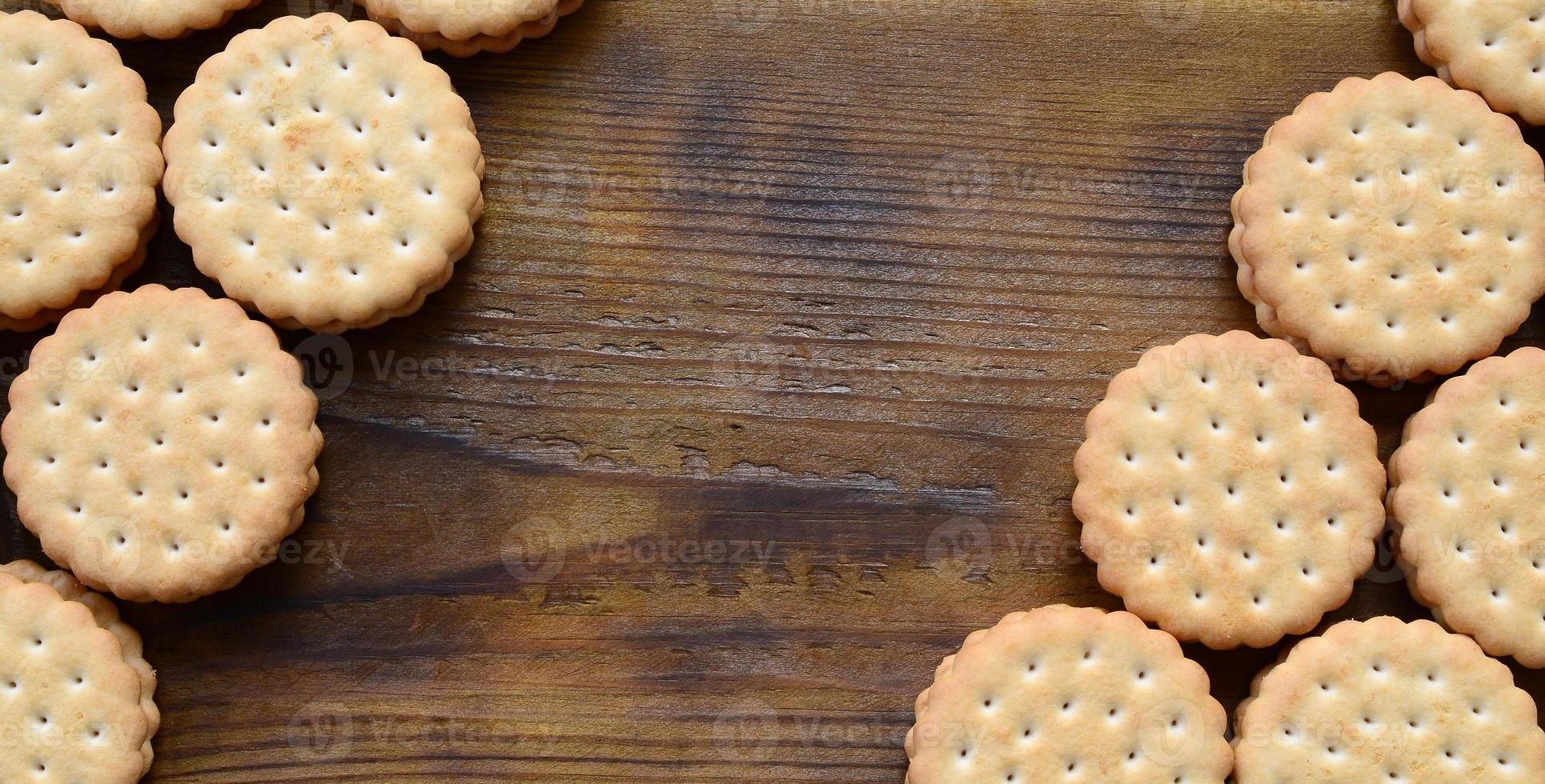 A round sandwich cookie with coconut filling lies in large quantities on a brown wooden surface. Photo of edible treats on a wooden background with copy space