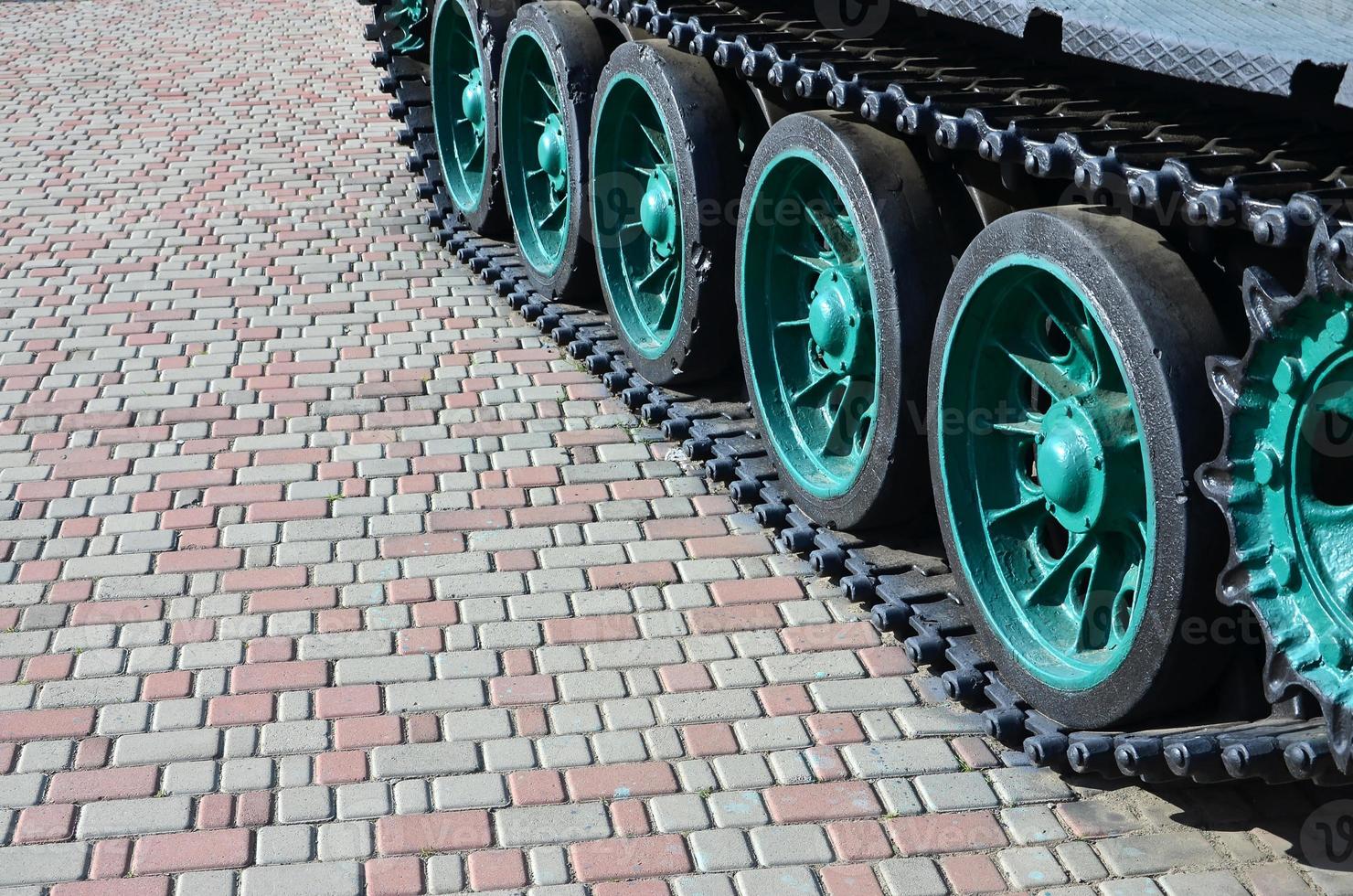 A military vehicle on caterpillar tracks stands on a square of paving stones. Photo of green caterpillars with metal wheels that rotate them