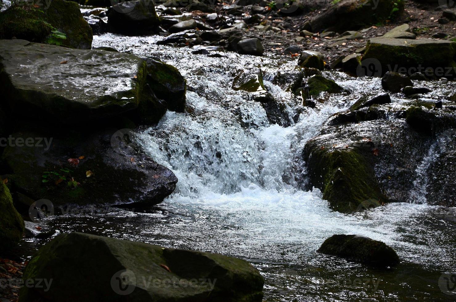 Close-up image of a small wild waterfall in the form of short streams of water between mountain stones photo