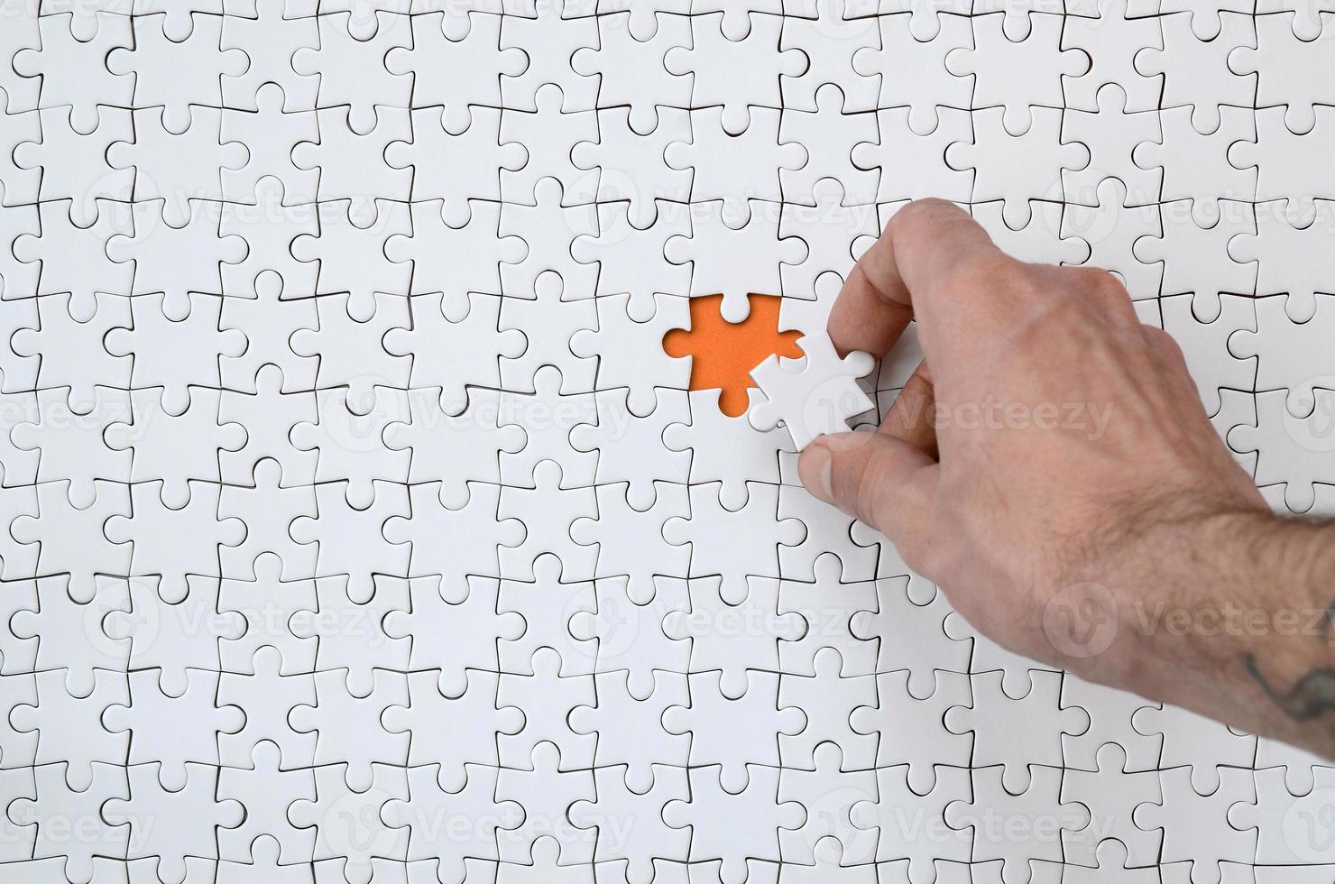 The texture of a white jigsaw puzzle in the assembled state with one missing element that the male hand puts in photo