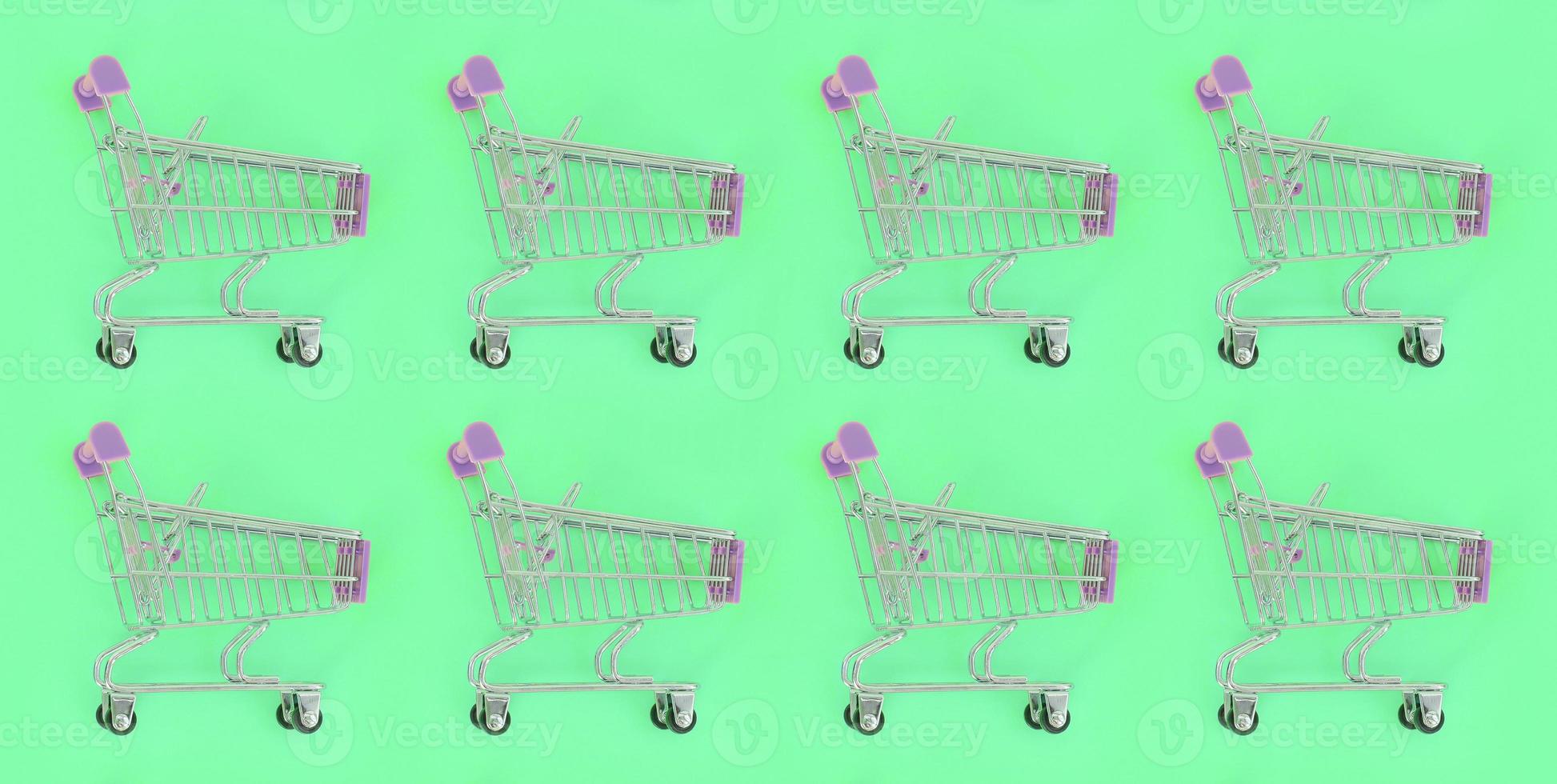 Shopping addiction, shopping lover or shopaholic concept. Many small empty shopping carts perform a pattern on a pastel colored paper background. Flat lay composition, top view photo