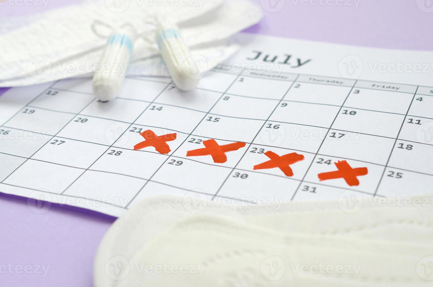 almohadillas menstruales y tampones en el calendario del período de menstruación con marcas de cruz roja sobre fondo lila foto