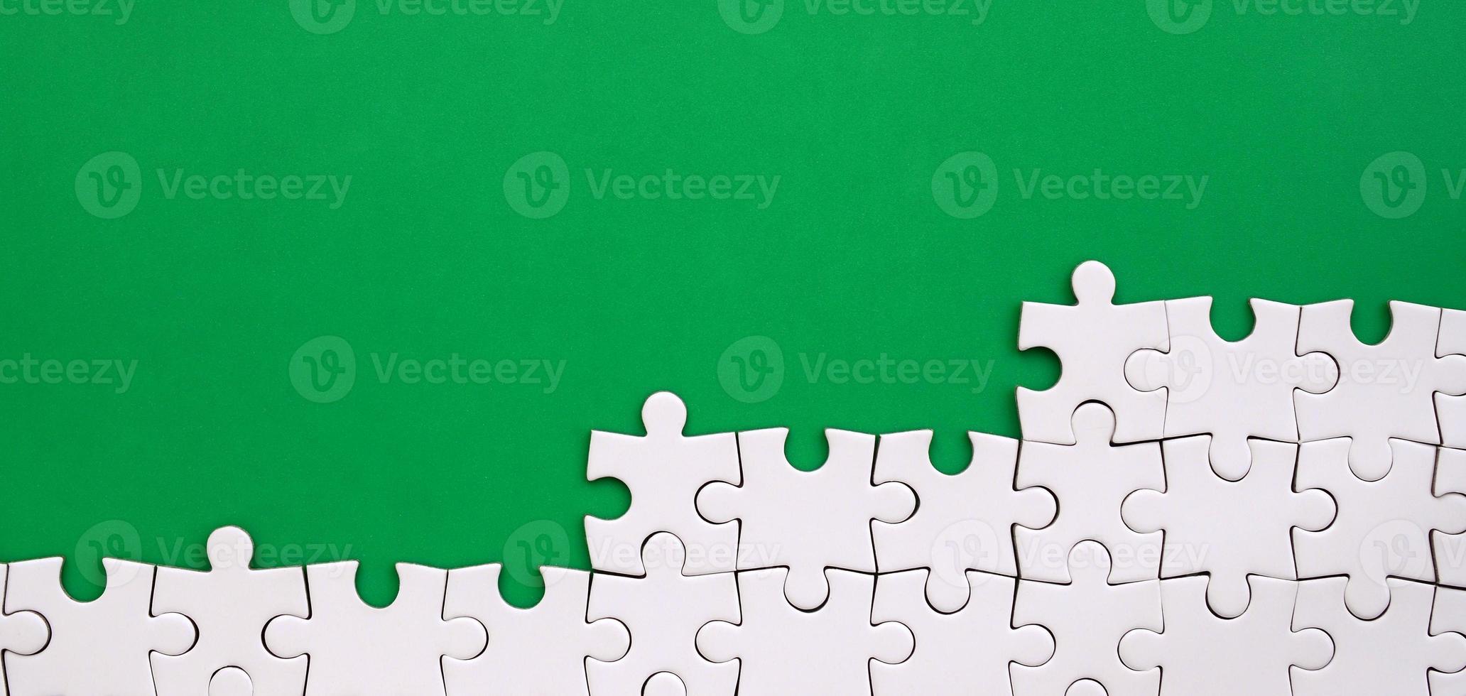 Fragment of a folded white jigsaw puzzle on the background of a green plastic surface. Texture photo with copy space for text