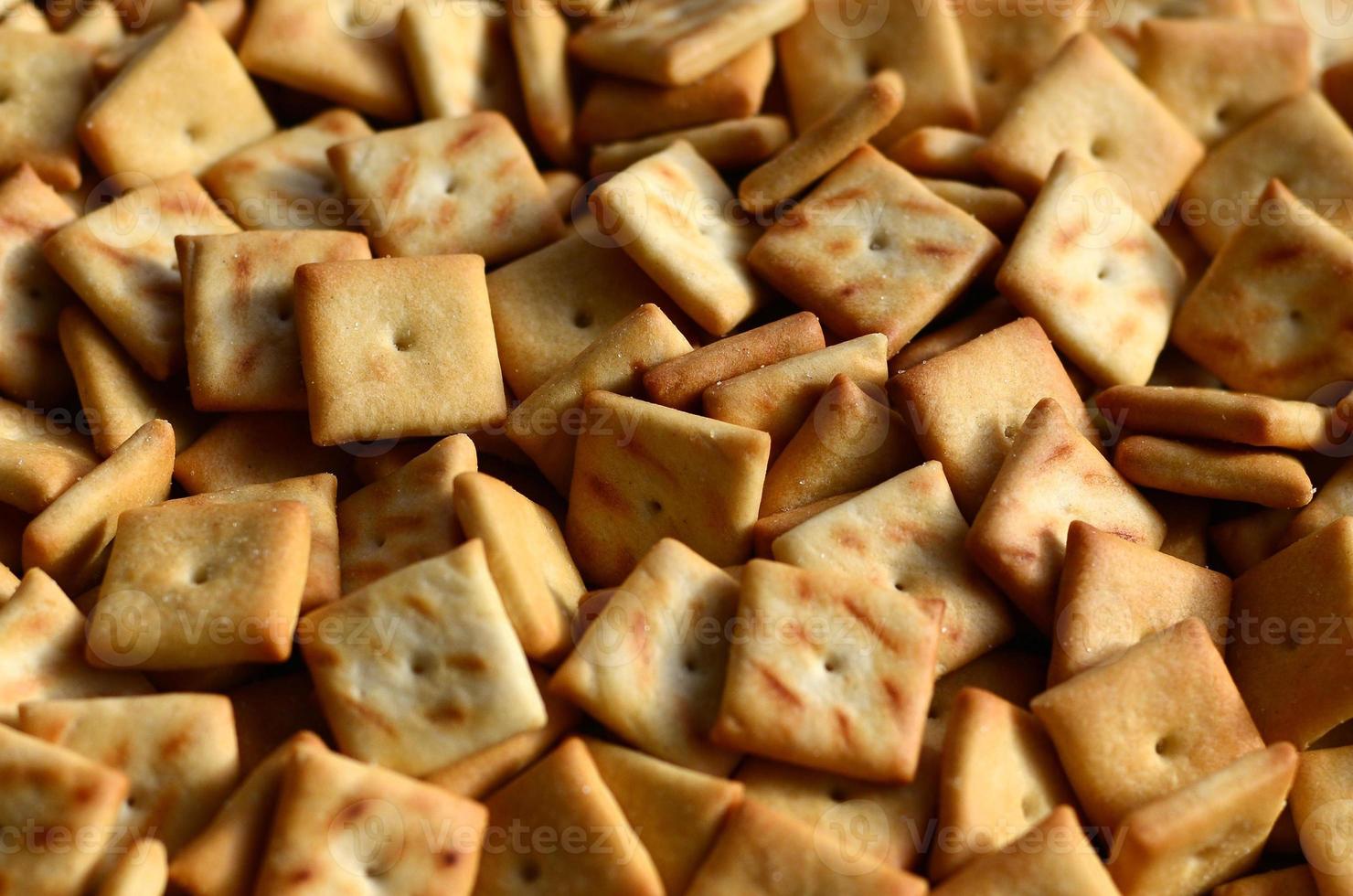 Background texture of small edible squares baked from dough and sprinkled with salt. A lot of salt cracker photo