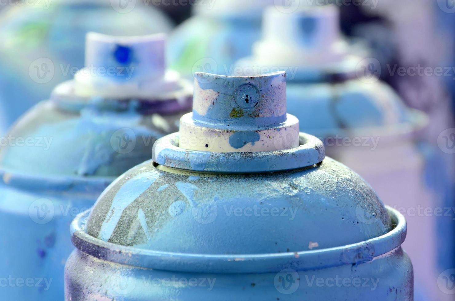 A lot of dirty and used aerosol cans of bright blue paint. Macro photograph with shallow depth of field. Selective focus on the spray nozzle photo