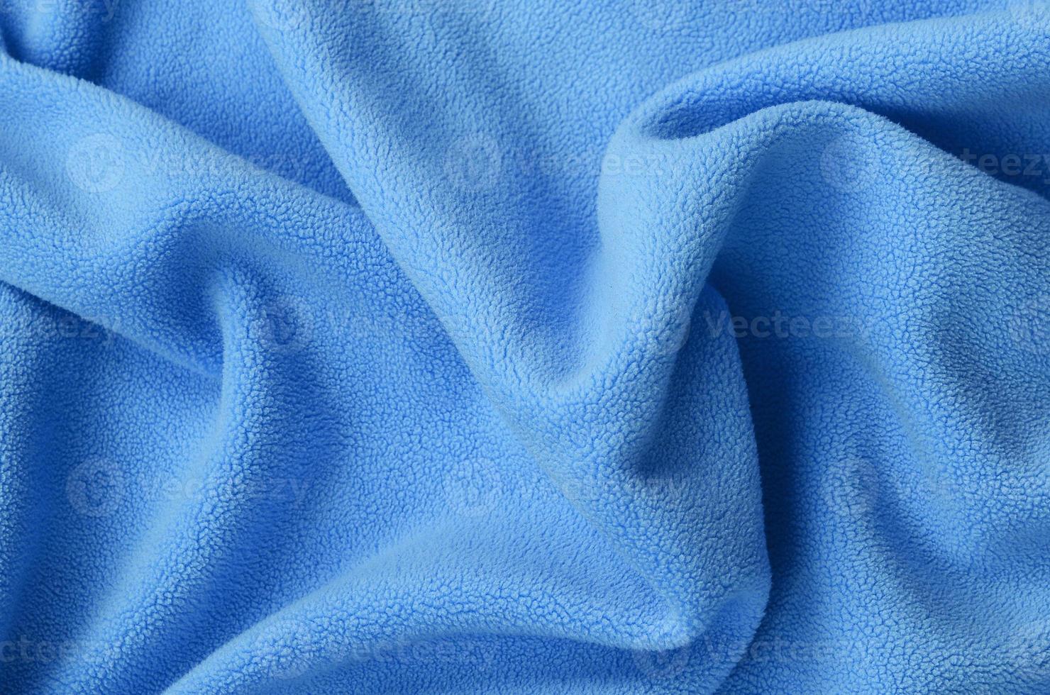 The blanket of furry blue fleece fabric. A background of light blue soft plush fleece material with a lot of relief folds photo
