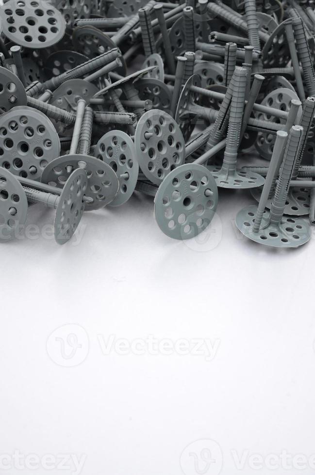 Background of many gray plastic dowels fastening for thermal insulation. A huge pile of plastic bolts with round holey hats lies on a gray foam polystyrene plate photo