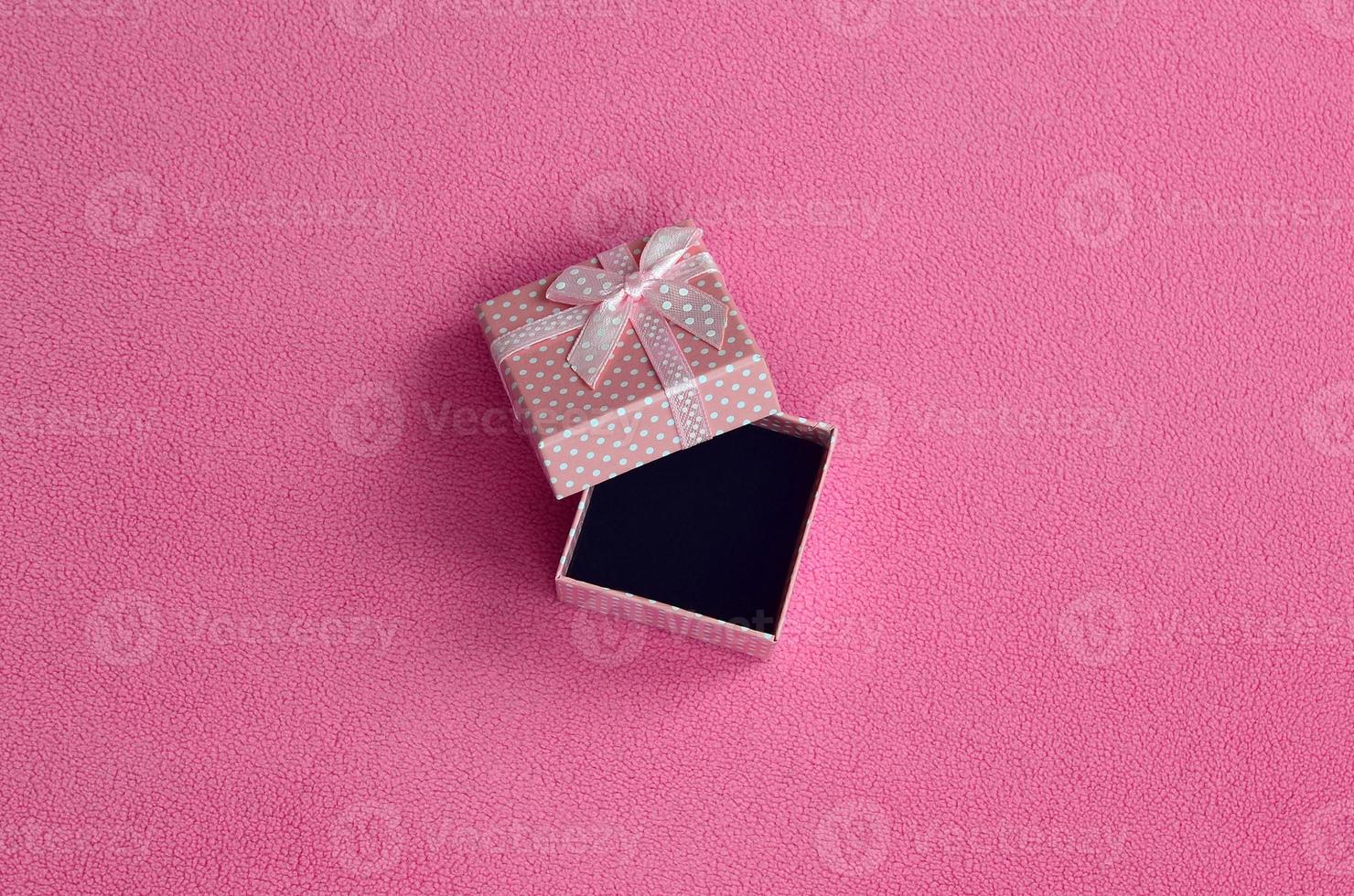 Open small gift box in pink with a small bow lies on a blanket of soft and furry light pink fleece fabric. Packing for a gift to your lovely girlfriend photo