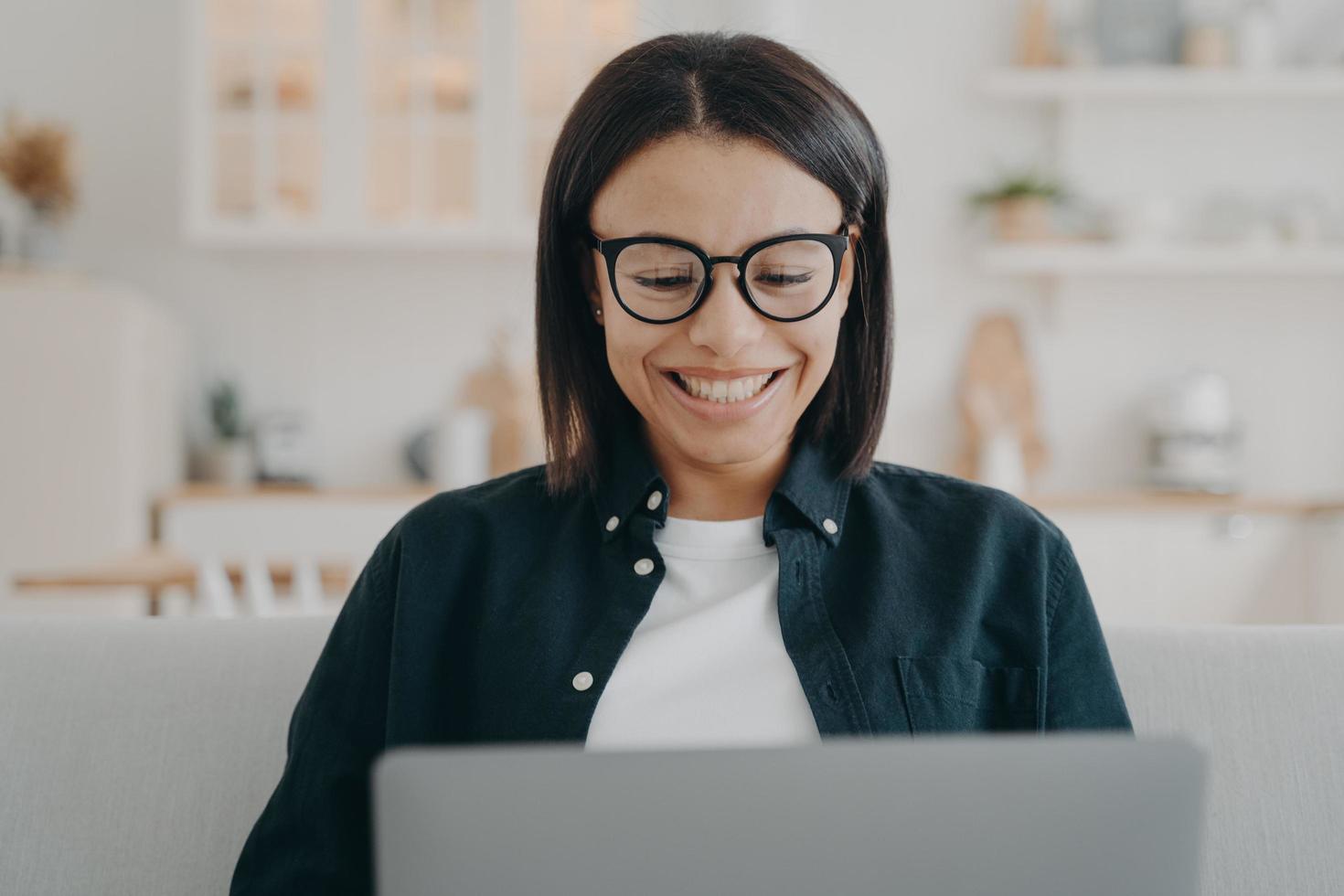 Smiling woman wearing glasses working or learning online at laptop at home. Remote job, elearning photo