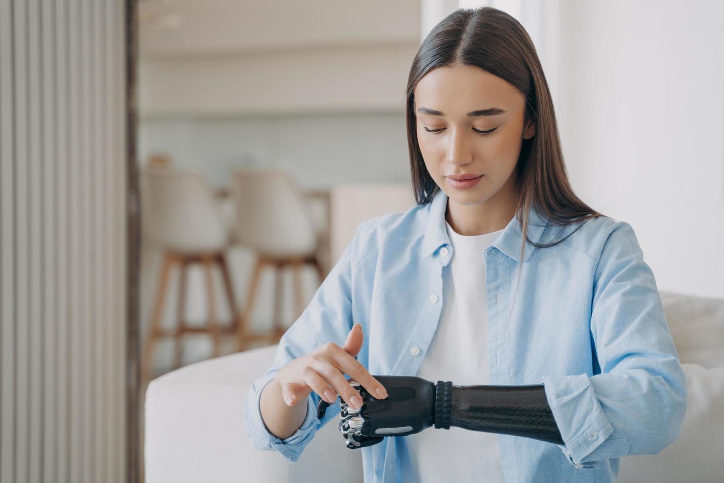 Beautiful young disabled girl with bionic prosthetic arm learning to turn on high tech prosthesis photo