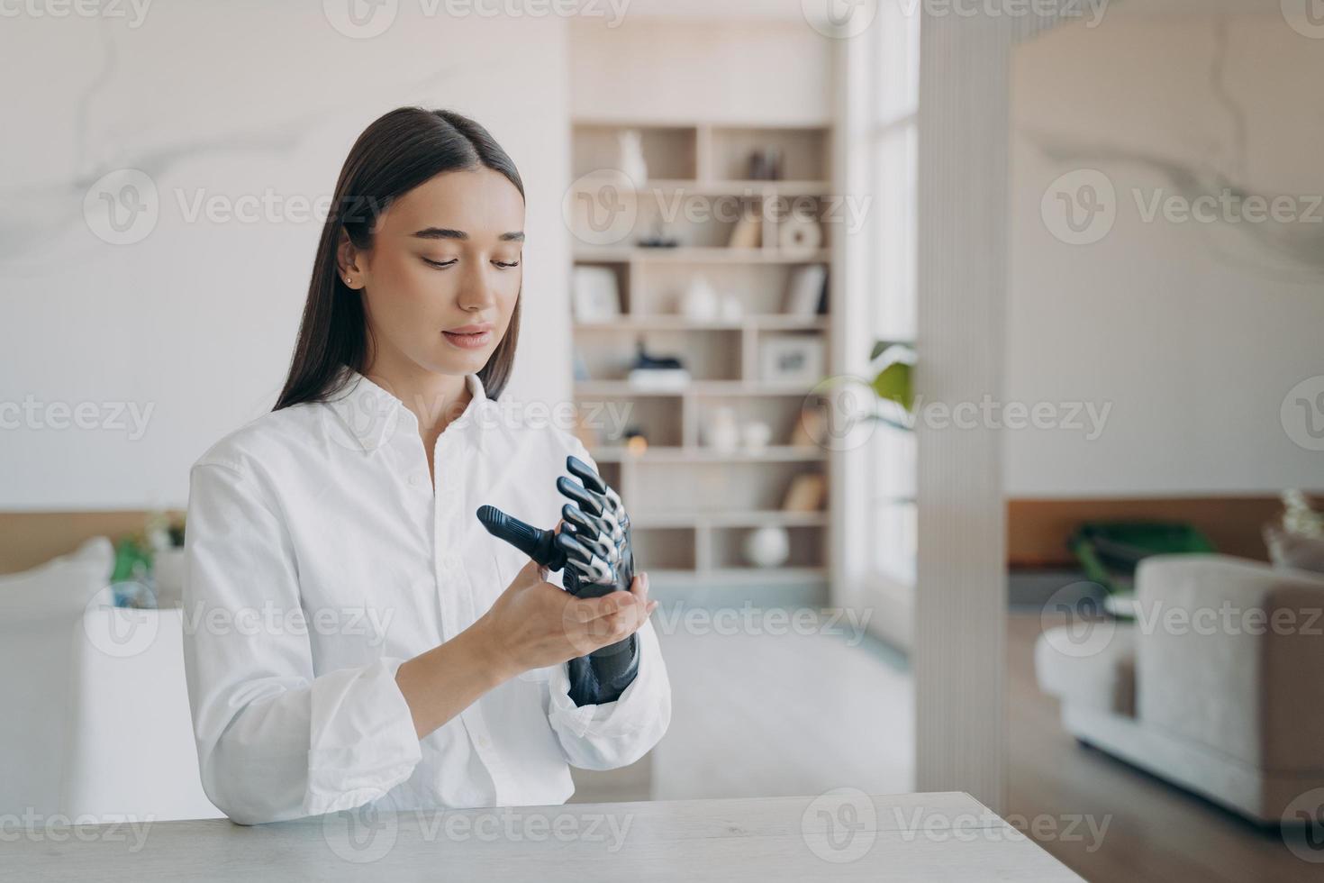 Modern disabled girl puts together modern lightweight bionic prosthetic arm sitting at table at home photo