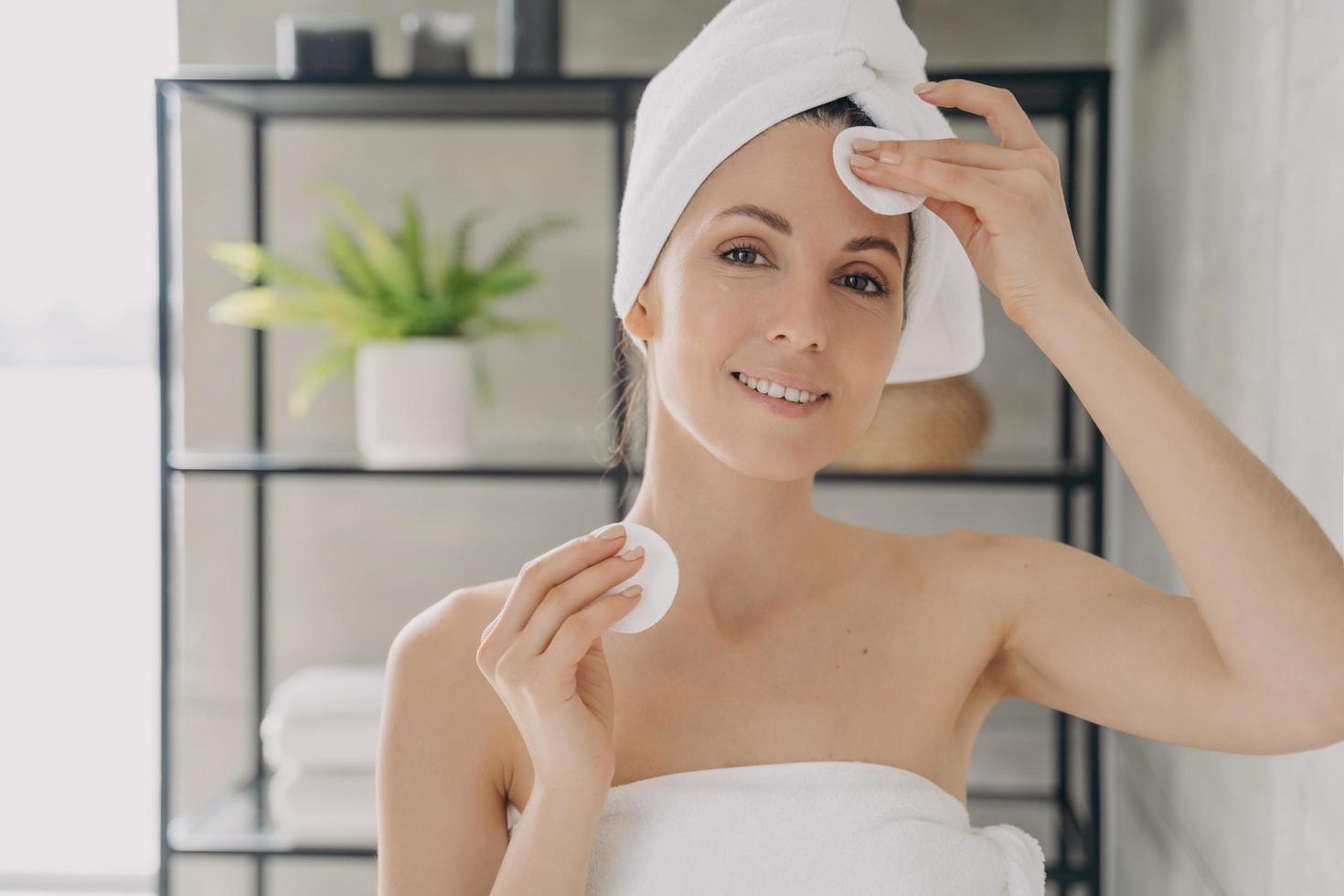 mujer hidratando, limpiando la piel del rostro, usando toallitas de algodón en el baño. higiene personal, cuidado de la piel foto