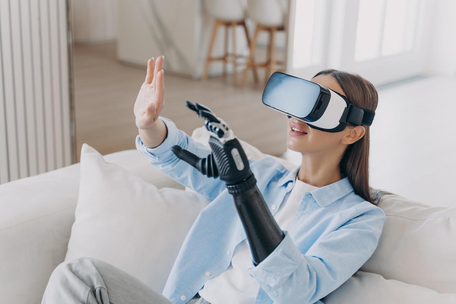 Girl with disability in VR glasses touching objects of virtual reality by bionic prosthetic arm photo