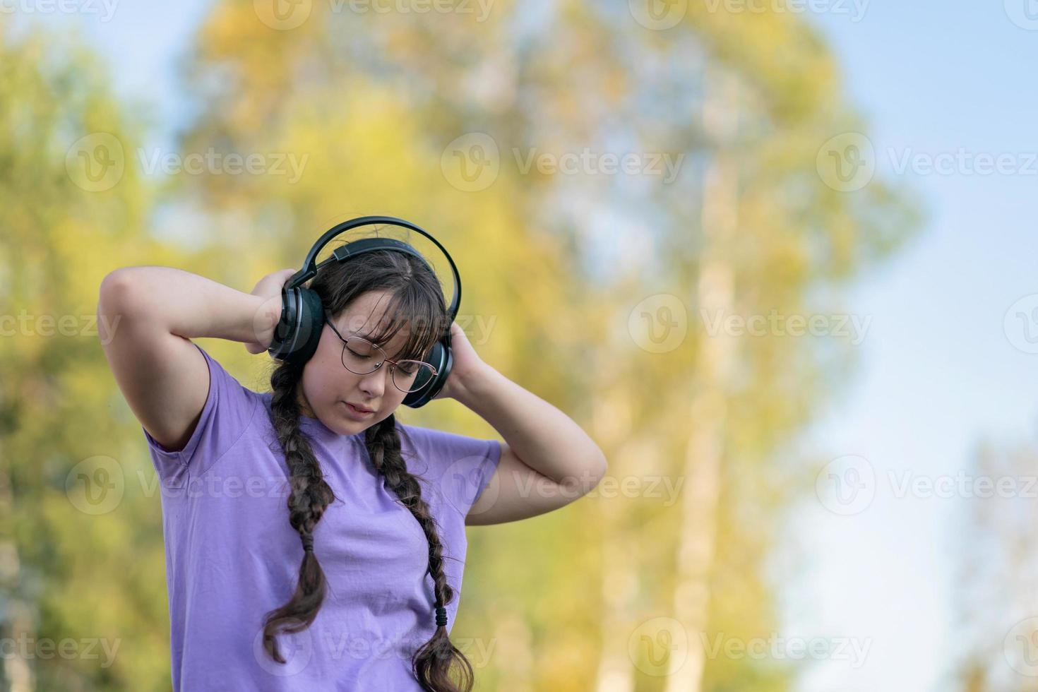 a teenager girl stands on the street, presses headphones to her ears with her hands and listens to music with her eyes closed. photo