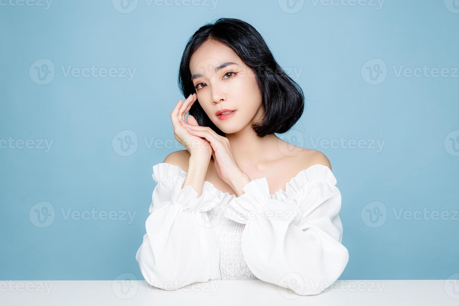 Asian woman short hair with Perfect clean fresh skin. Cute female model with natural makeup and sparkling eyes on blue isolated background. Facial treatment, Cosmetology, beauty Concept. photo