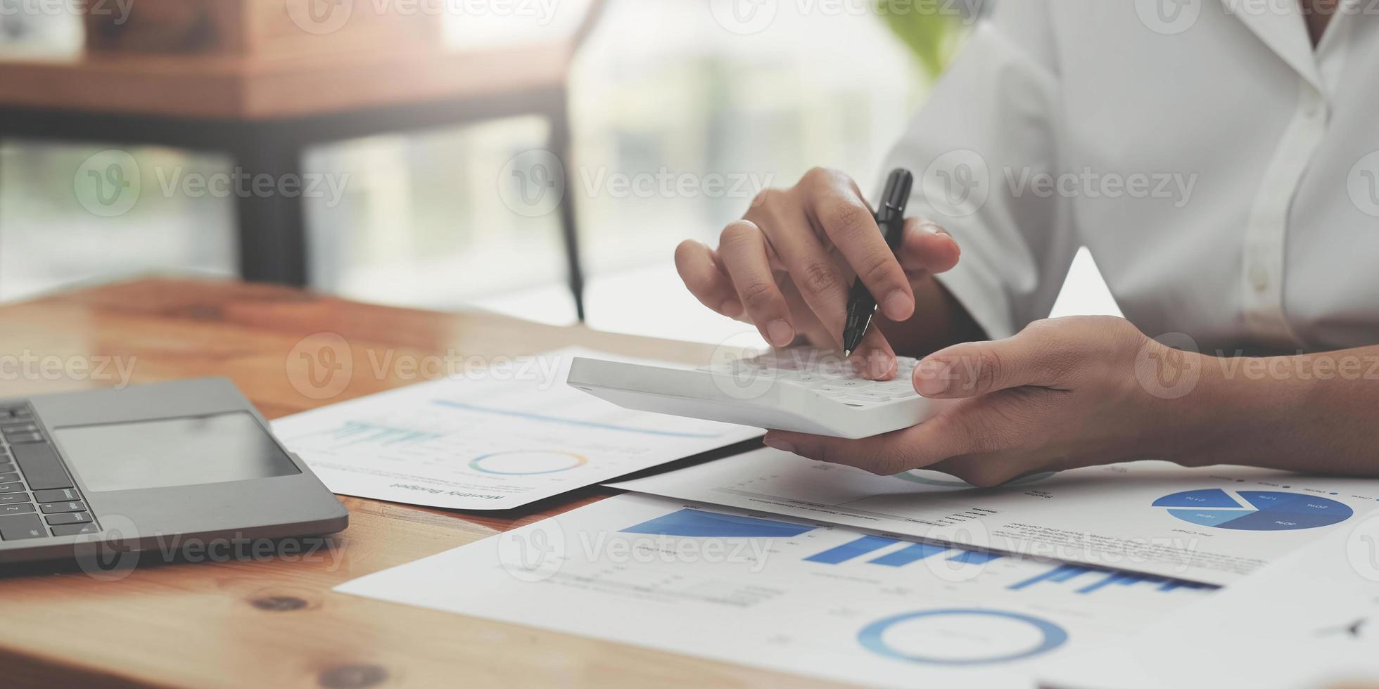 woman hand using calculator, working with graph chart and analyzing business strategy, financial statistic, sitting at desk office, vertical view. photo