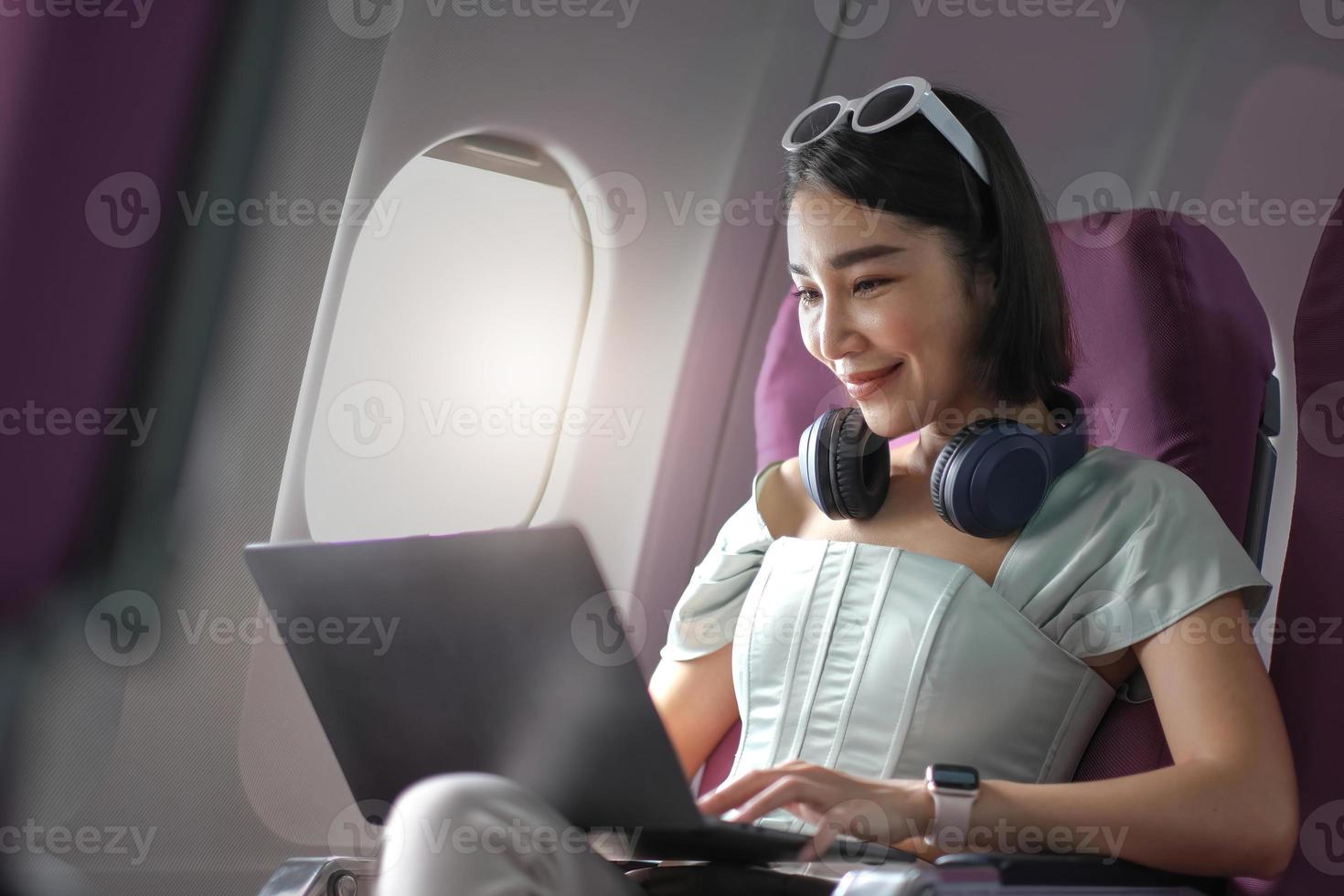 mujer joven asiática que usa una computadora portátil sentada cerca de las ventanas en primera clase en un avión durante el vuelo, los viajes y el concepto de negocios foto