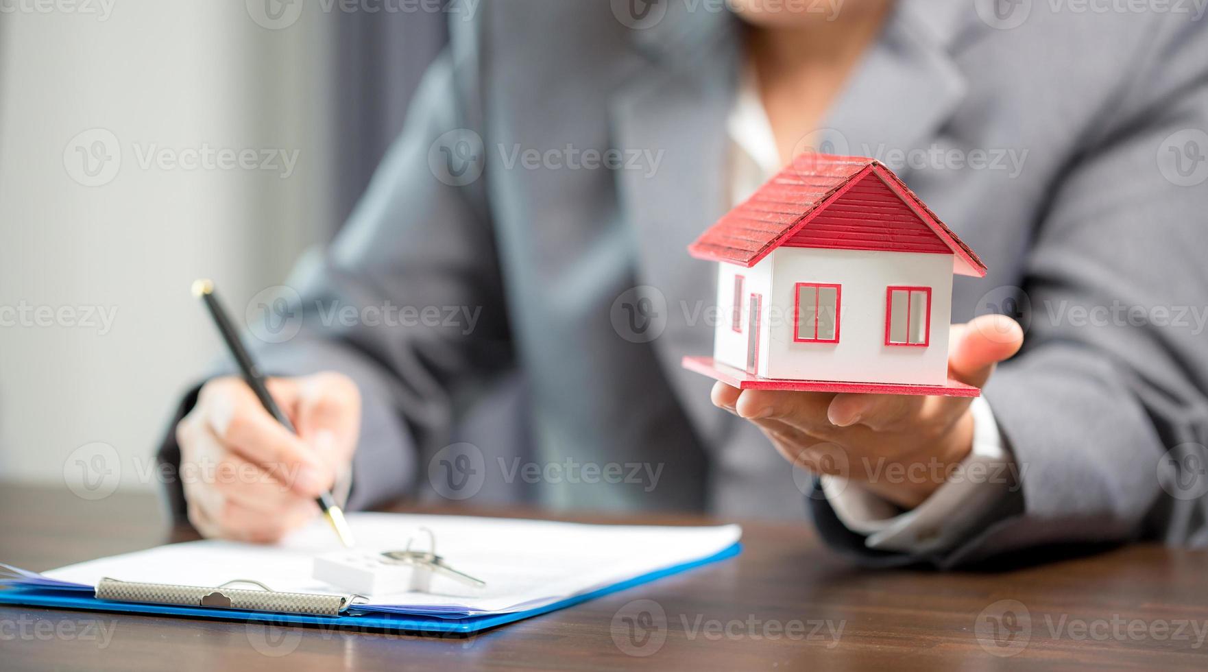 Woman home sales person is checking documents for house purchase contract before letting the customer sign contract on table is key with house model, real estate trading and insurance property concept photo