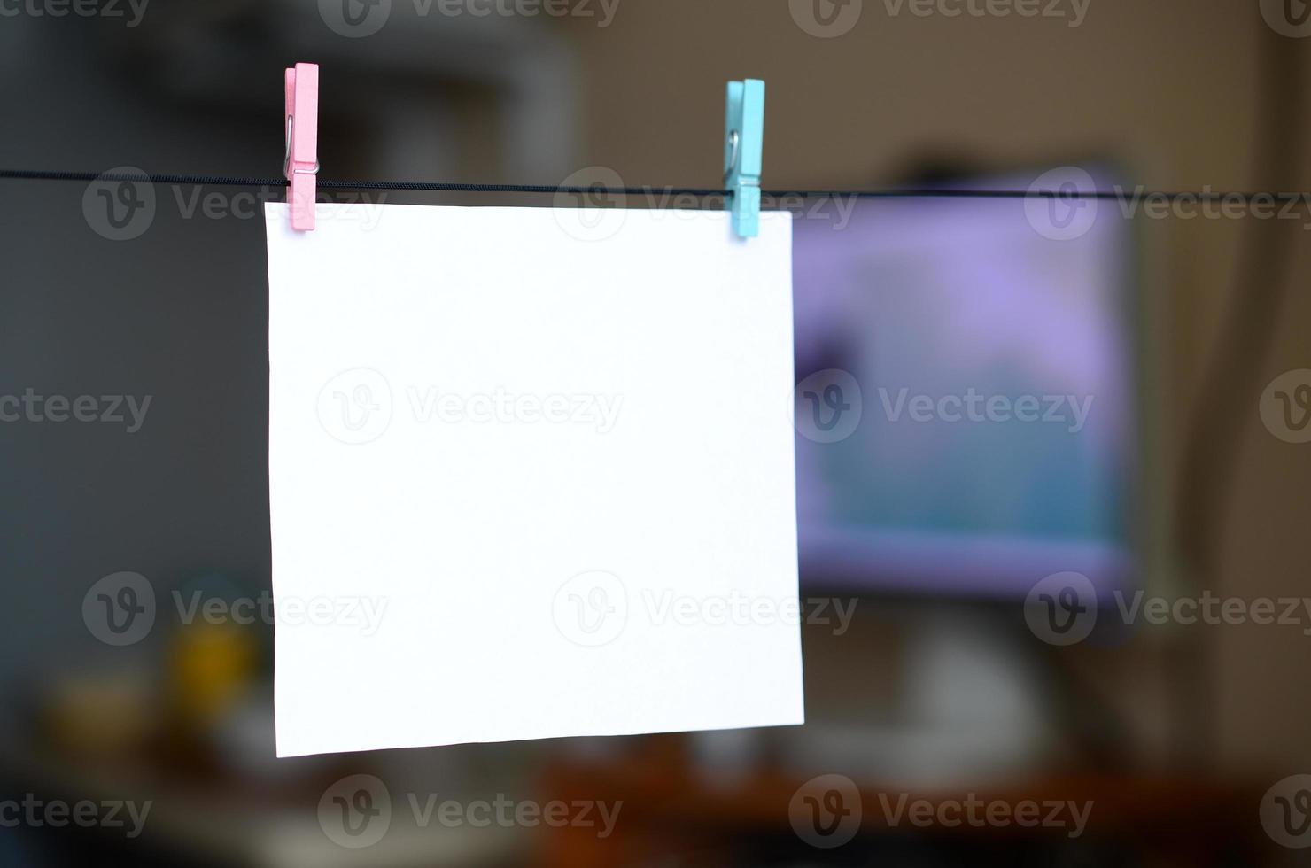 White blank card on rope, dark office background. Creative reminder, small sheet of paper on wooden clothespin, memo backdrop photo