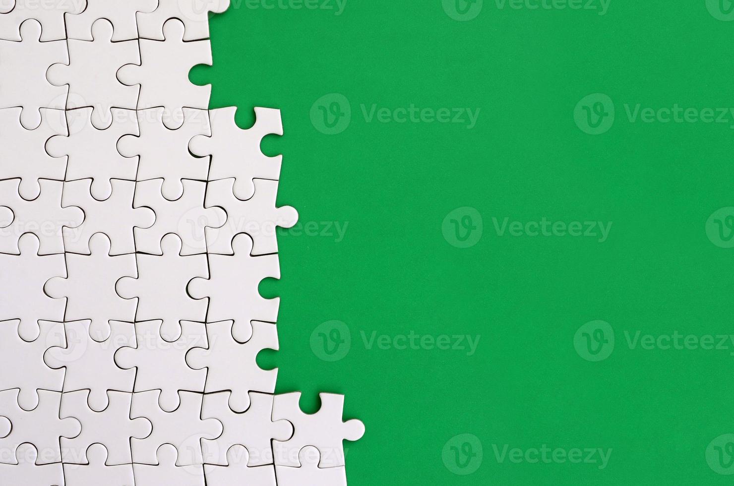 Fragment of a folded white jigsaw puzzle on the background of a green plastic surface. Texture photo with copy space for text