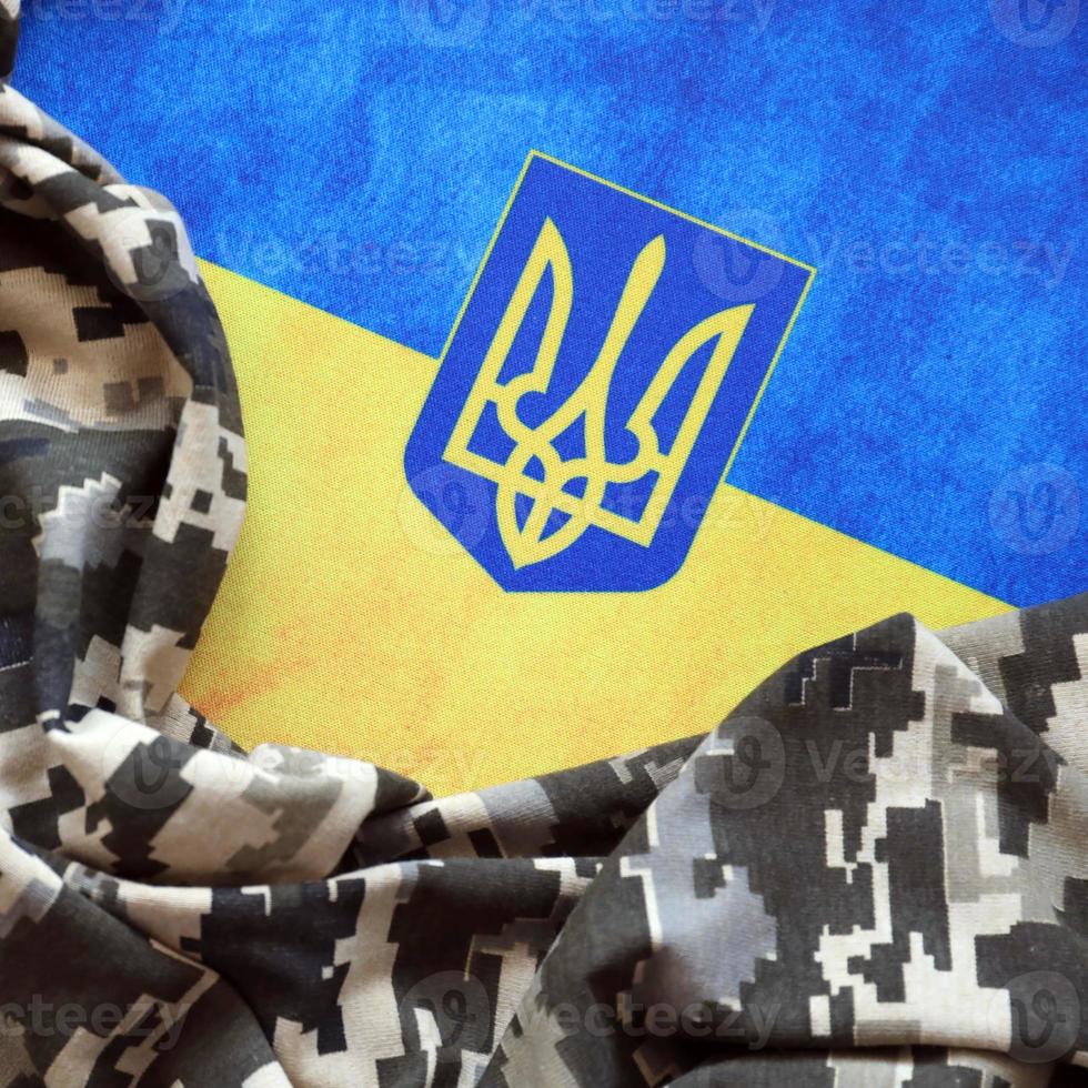 bandera ucraniana y escudo de armas con tela con textura de camuflaje pixelado. tela con patrón de camuflaje en formas de píxeles grises, marrones y verdes con signo de tridente ucraniano foto